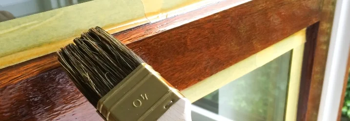 Person streicht Holzfenster mit Pinsel